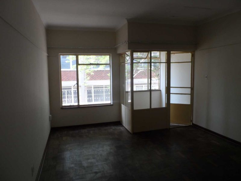 An empty living room featuring original parquet flooring and an enclosed balcony area with glass partitioning, offering a blank canvas for renovation.