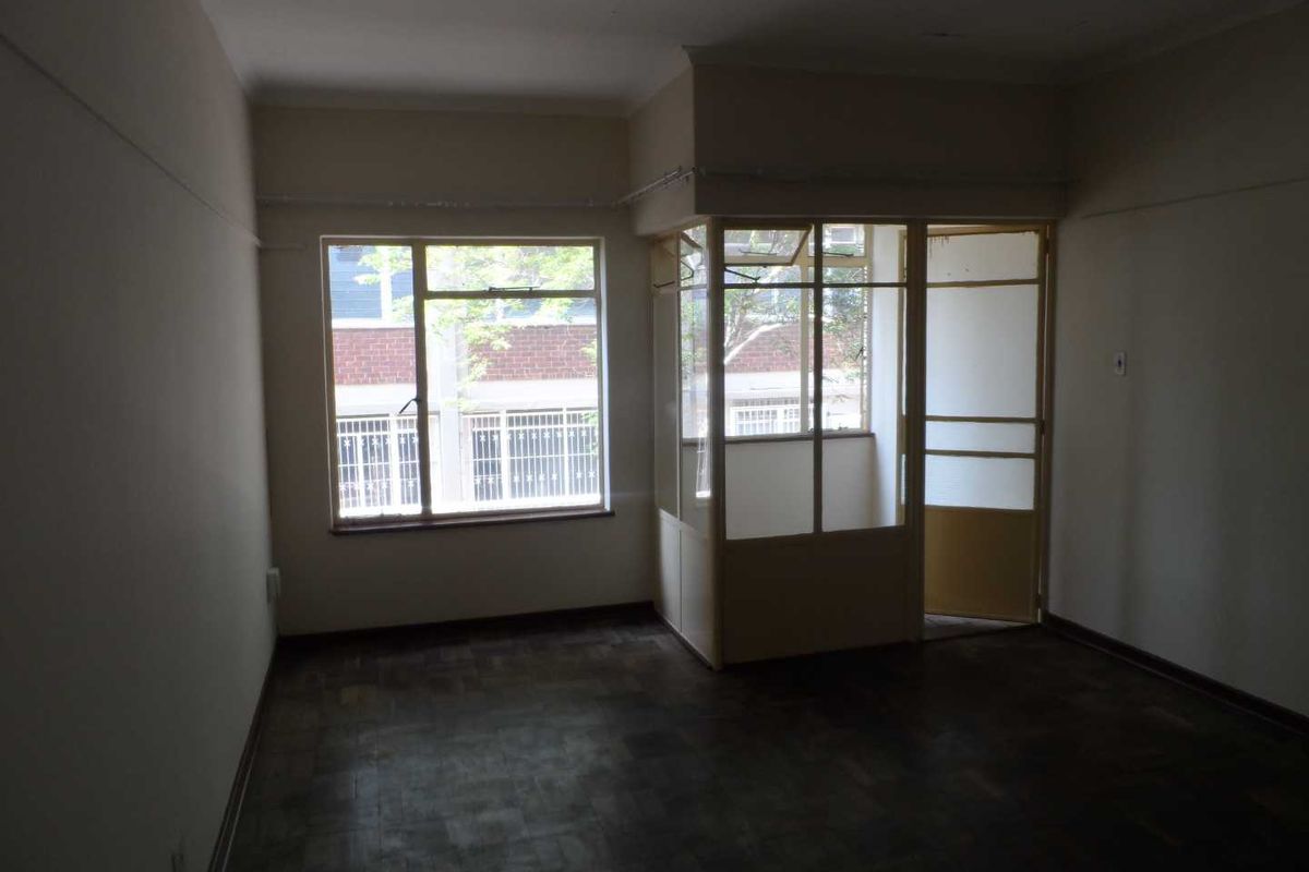 An empty living room featuring original parquet flooring and an enclosed balcony area with glass partitioning, offering a blank canvas for renovation.