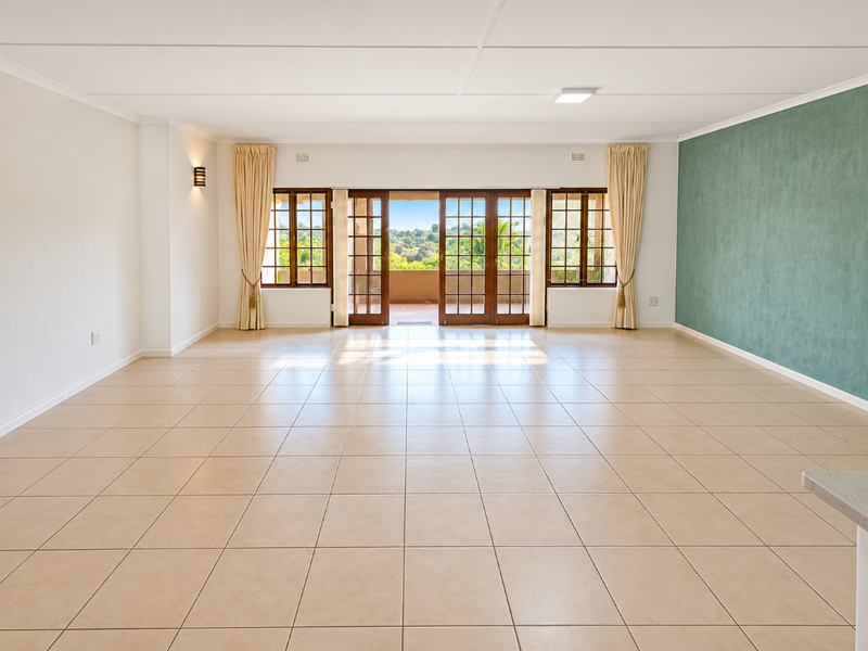 Spacious, light-filled living area featuring neutral ceramic tile flooring, a green accent wall, and large wooden sliding doors opening to an outdoor balcony.
