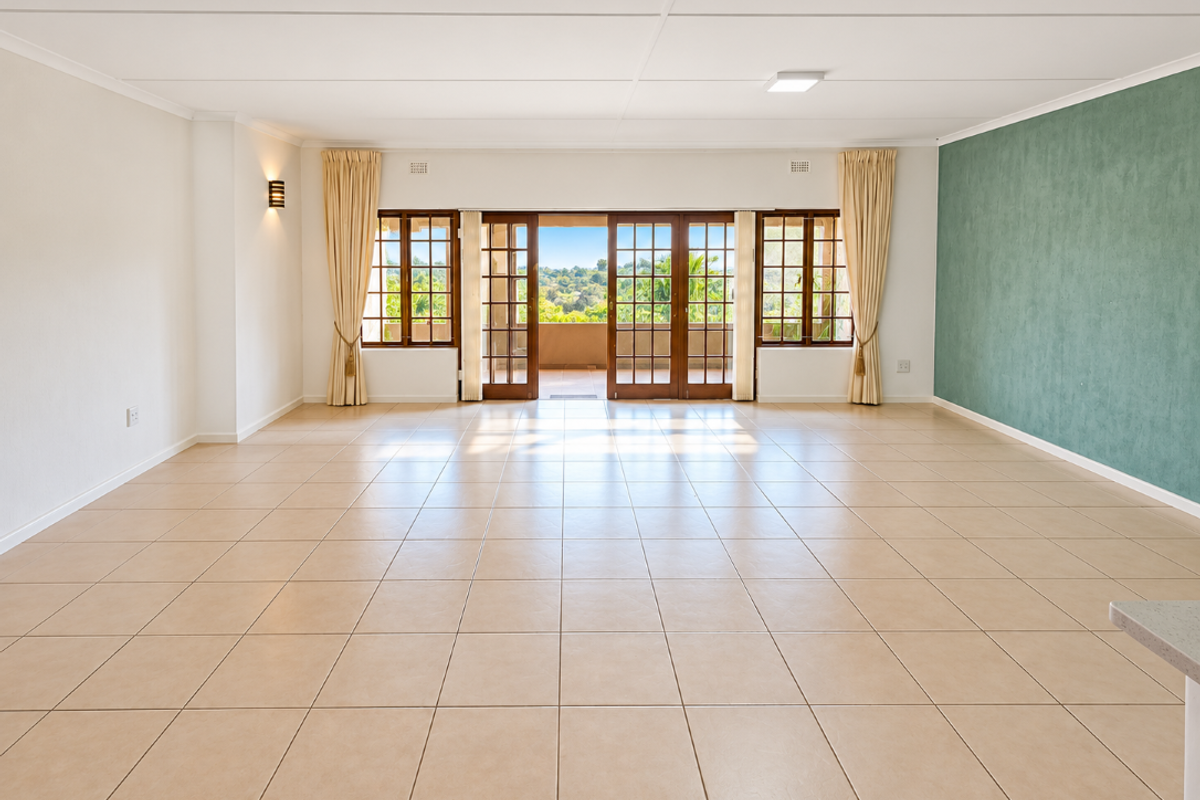 Spacious, light-filled living area featuring neutral ceramic tile flooring, a green accent wall, and large wooden sliding doors opening to an outdoor balcony.