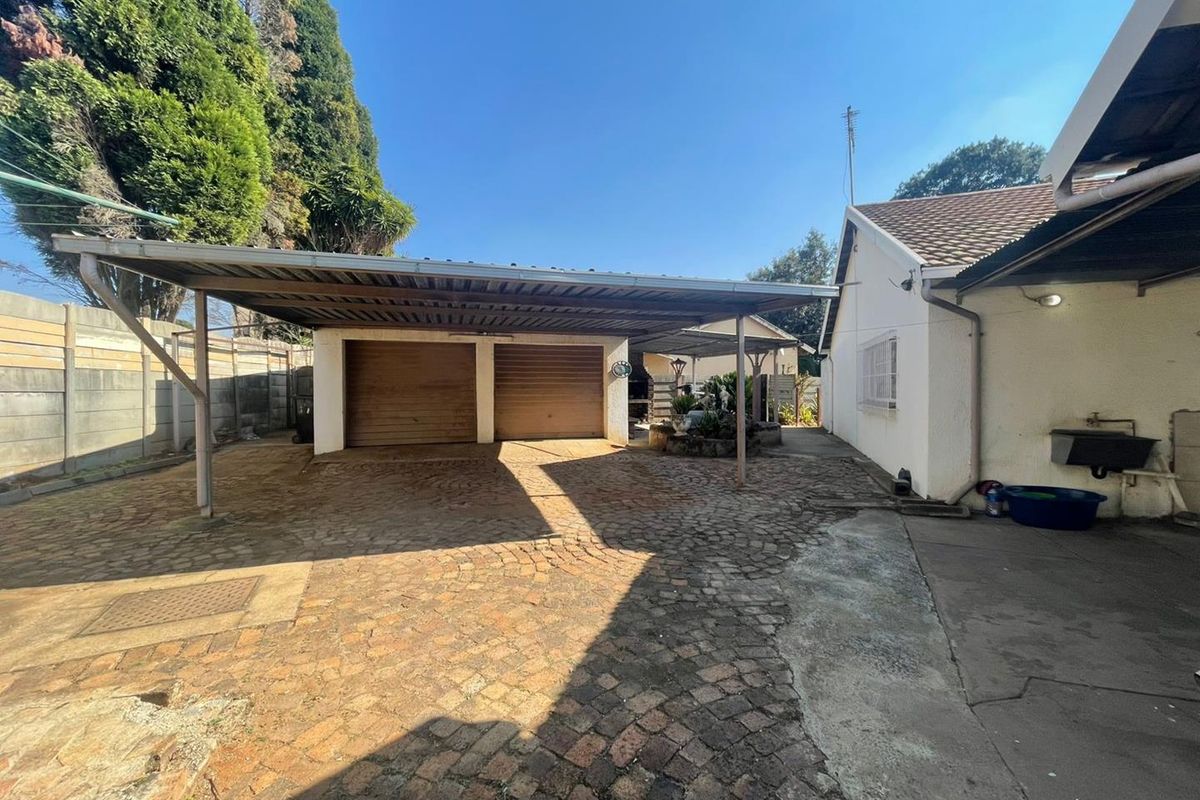 Rear exterior view featuring a double garage, covered carport, paved driveway, and an external wash basin area.