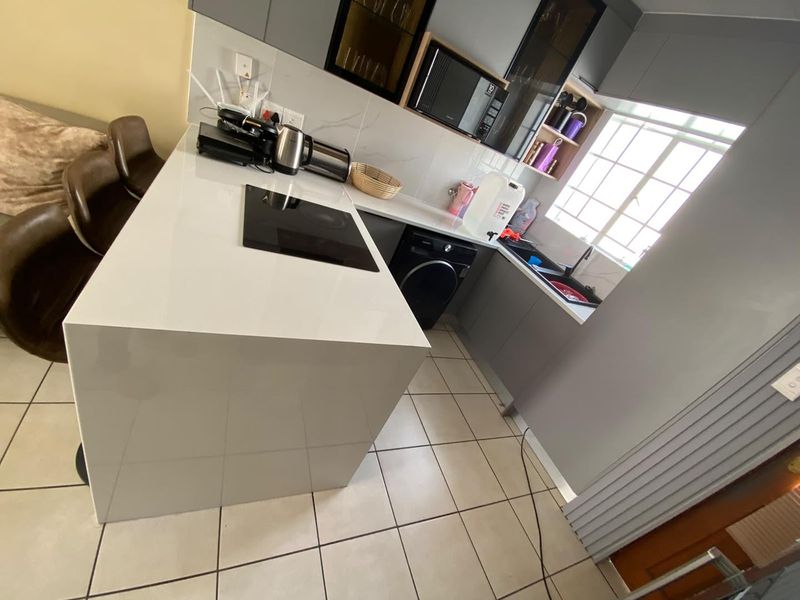 Modern kitchen featuring a central island with a built-in hob, sleek grey cabinetry, built-in microwave, and tiled flooring.