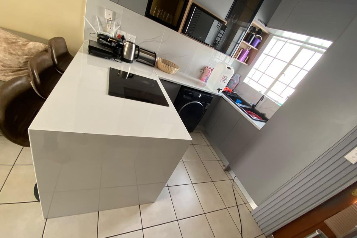 Modern kitchen featuring a central island with a built-in hob, sleek grey cabinetry, built-in microwave, and tiled flooring.