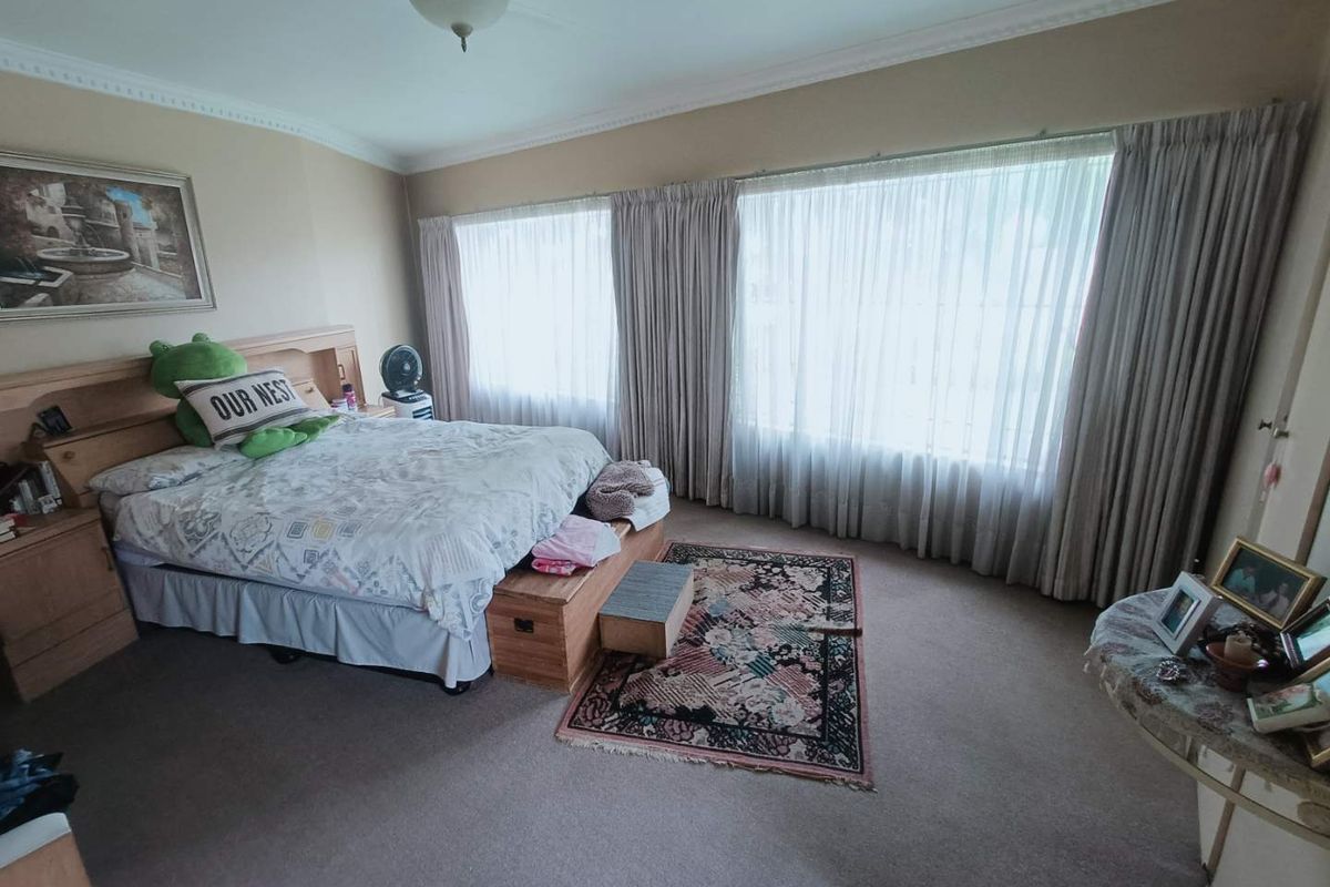 Spacious bedroom featuring large windows with floor-to-ceiling curtains, neutral carpeting, and decorative crown molding.