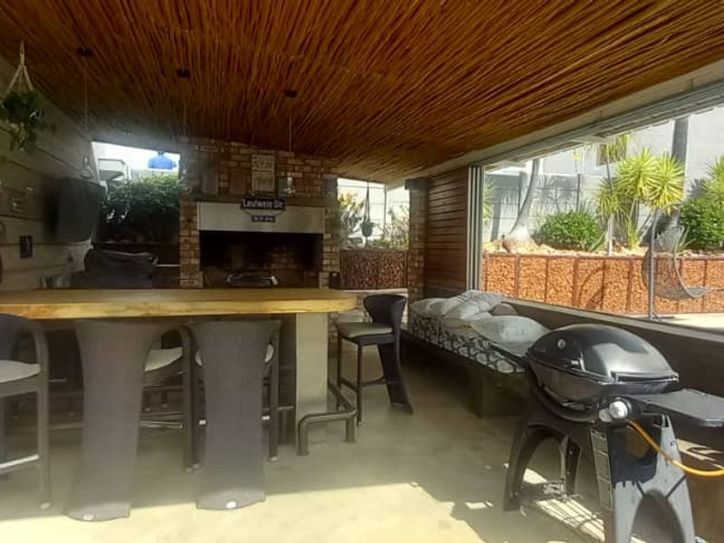 Covered outdoor entertainment area featuring a built-in braai, timber ceiling, and brick pillars, overlooking the pool area.