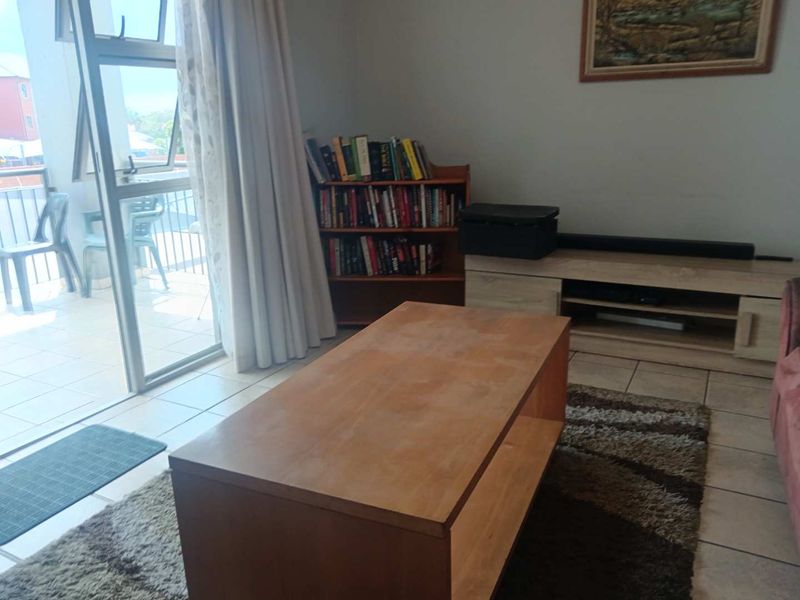 A living room area featuring tiled flooring and a sliding glass door providing direct access to an outdoor balcony.