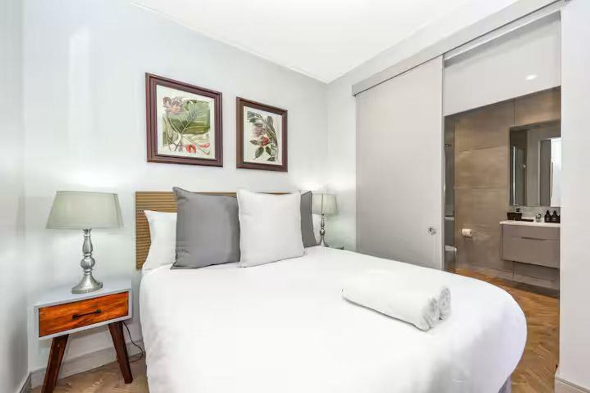 A modern bedroom featuring herringbone flooring and a sliding door leading to a contemporary en-suite bathroom with a sleek vanity.