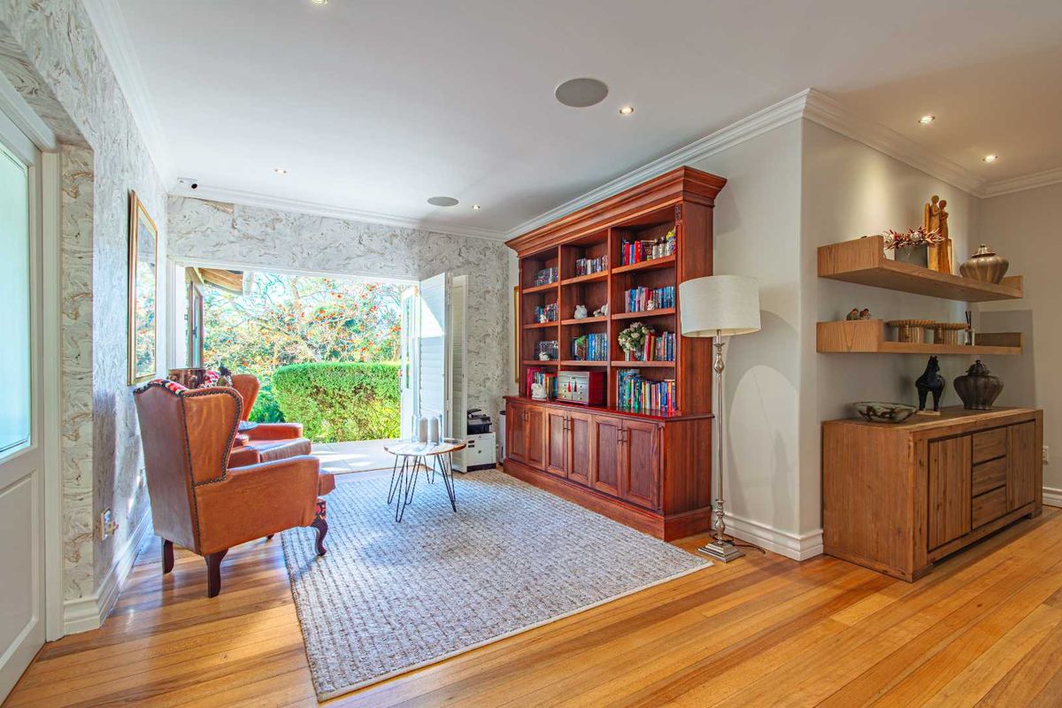 A cozy living area featuring polished hardwood floors, a large built-in wooden bookshelf, recessed lighting, and direct access to the garden through french doors.