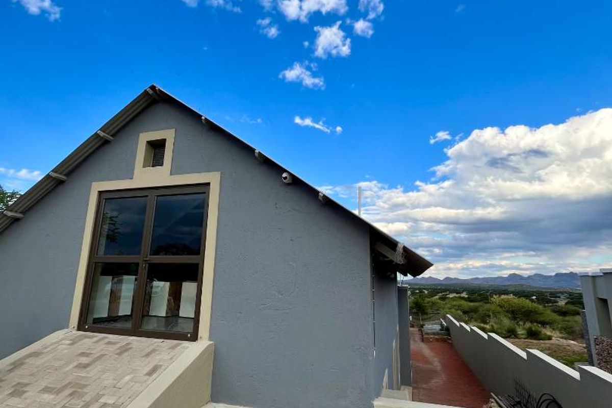 Exterior view of the property featuring a paved entrance ramp, grey rendered facade, and a large window overlooking the surrounding landscape.