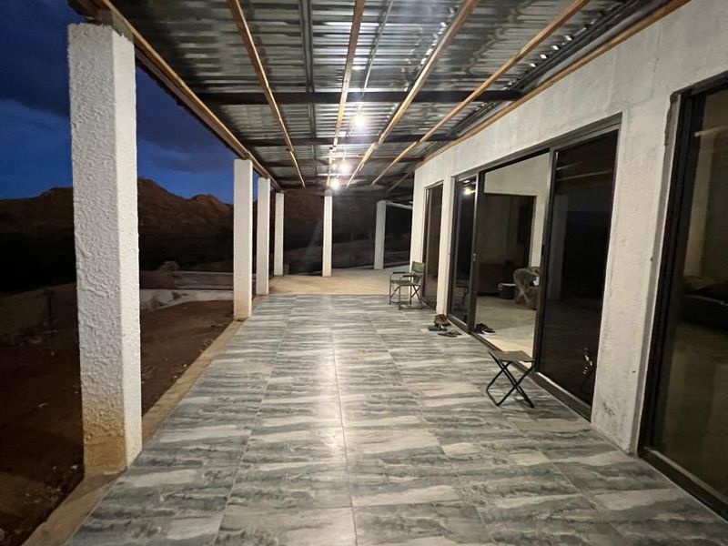 A spacious covered patio featuring tiled flooring, concrete support pillars, and sliding glass doors, offering an expansive outdoor entertainment area with mountain views.