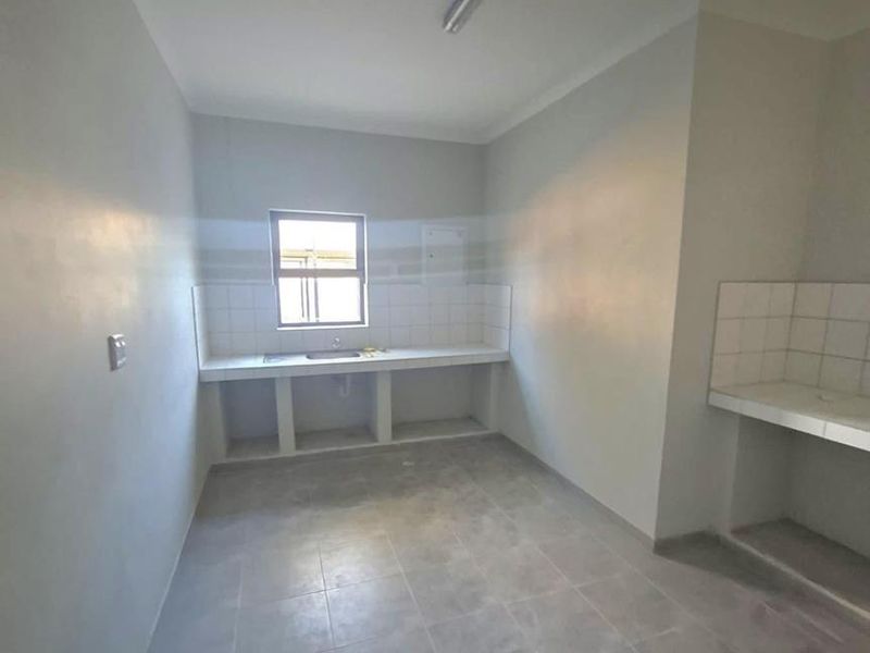 A basic, empty kitchen area featuring tiled countertops, a built-in sink, and tiled flooring, requiring finishing touches to complete the space.