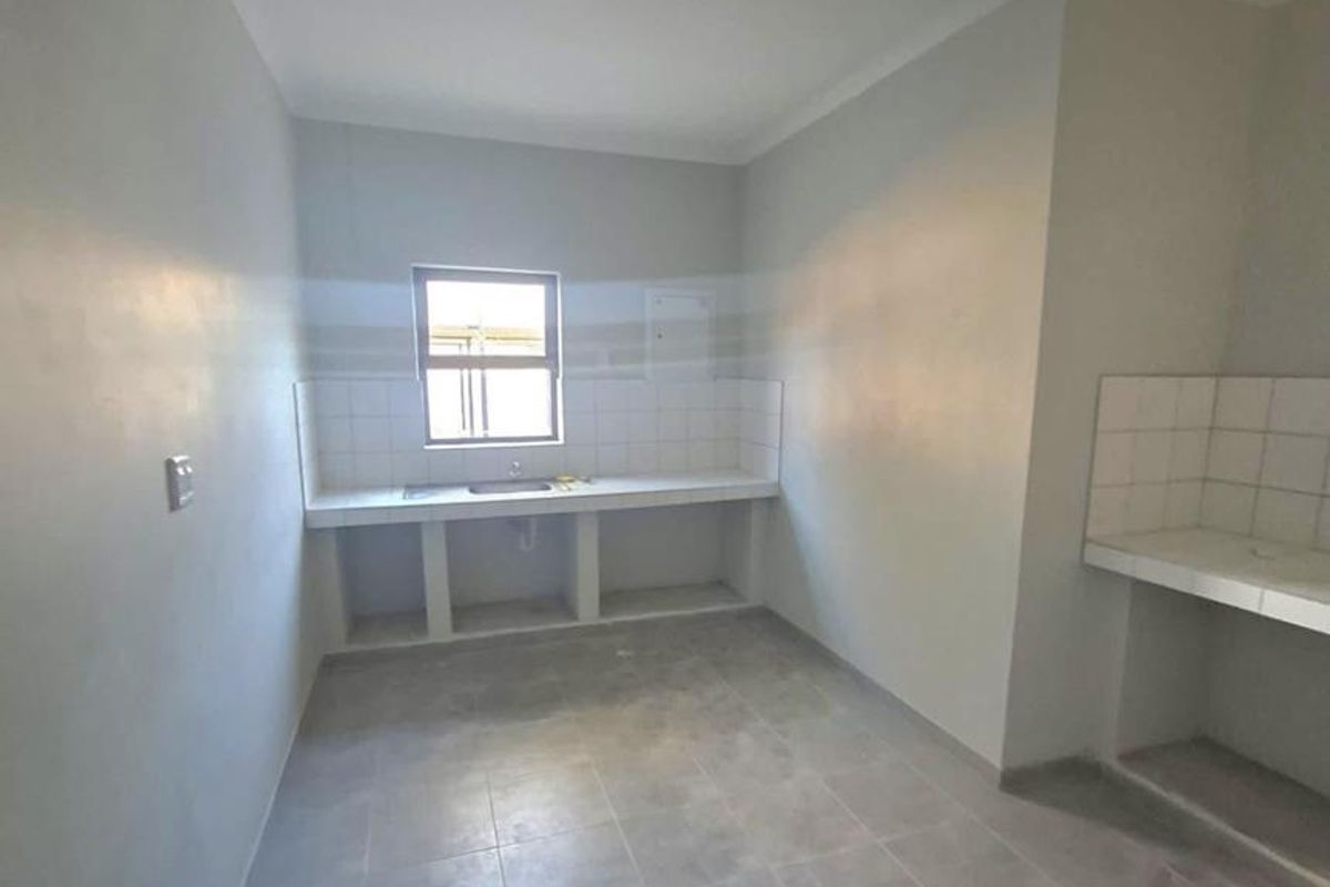 A basic, empty kitchen area featuring tiled countertops, a built-in sink, and tiled flooring, requiring finishing touches to complete the space.