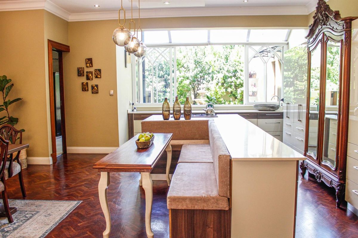 A well-appointed kitchen featuring custom cabinetry, stone countertops, integrated cooktop, and elegant parquet flooring, illuminated by natural light from a large window.