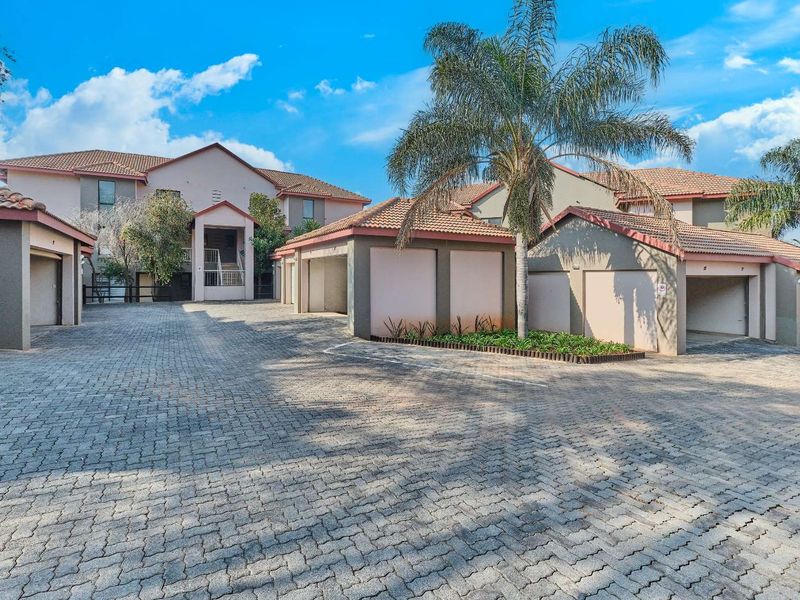 Front view of the townhouse complex featuring a paved driveway, multiple garage units, and well-maintained exterior building facades with tiled roofing.
