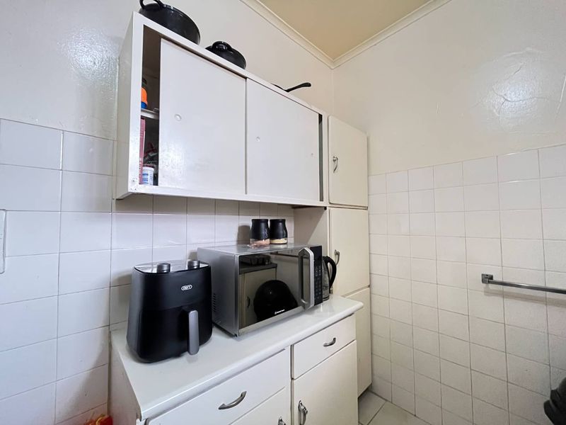 A compact kitchen area featuring white built-in cabinetry and tiled wall finishes, providing functional storage and preparation space.