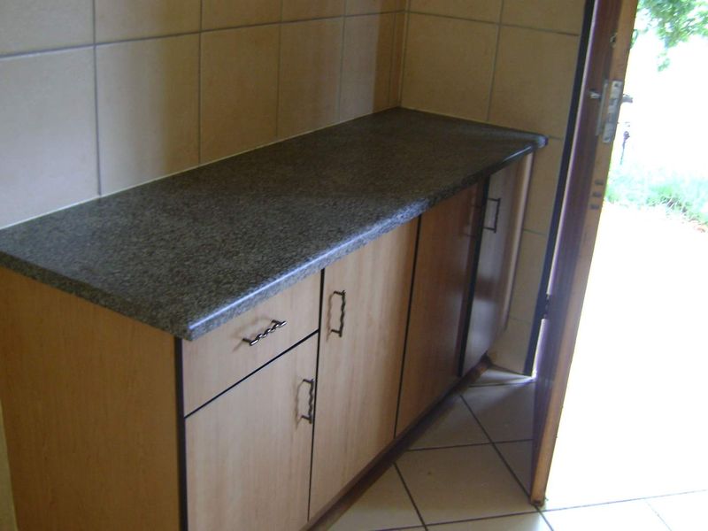 A functional scullery or utility area featuring laminate cabinetry, durable countertops, and tiled finishes, providing convenient access to the exterior.