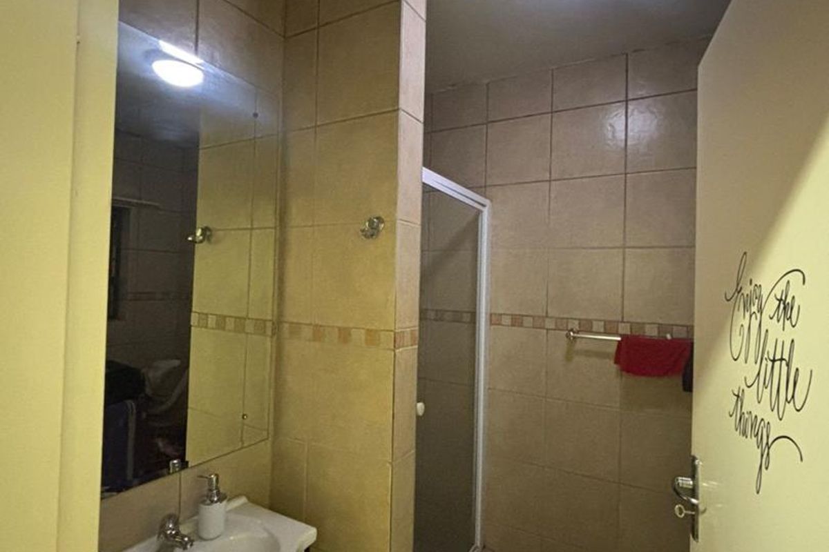 A functional bathroom featuring a vanity basin, a glass-enclosed shower, and neutral wall tiling.