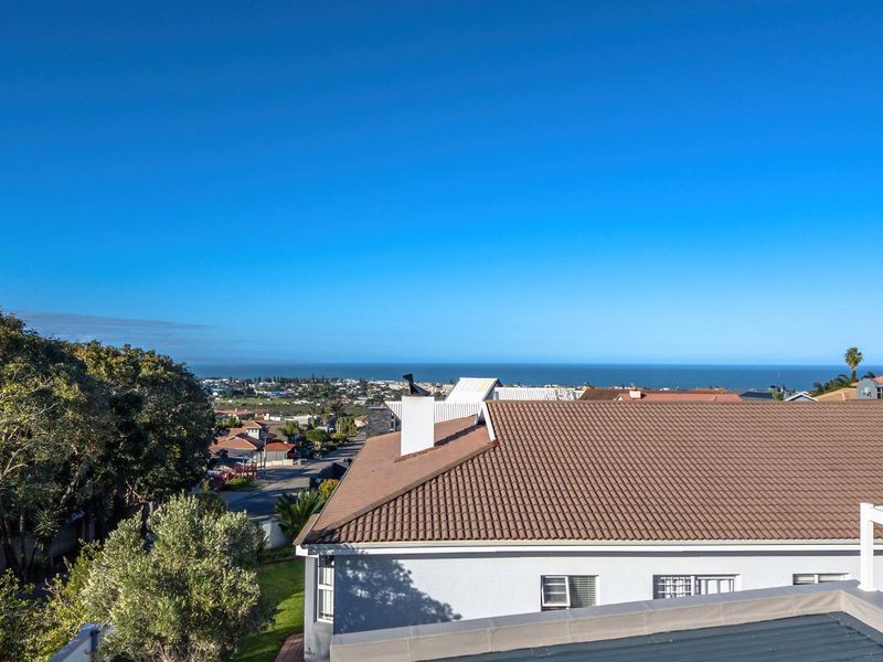 Elevated aerial view showcasing the property roofline, surrounding residential neighborhood, and expansive coastal ocean horizon.