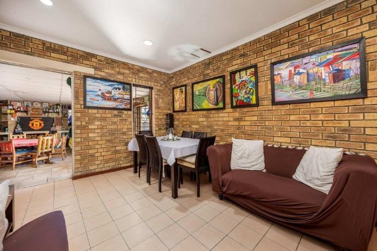 A living and dining area featuring exposed face-brick walls, tiled flooring, and recessed ceiling lighting, providing a rustic and functional living space.