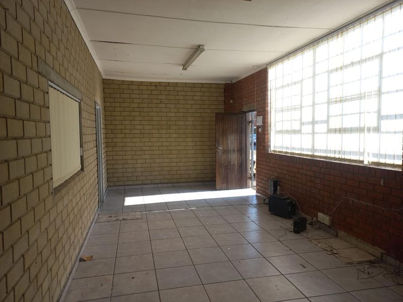An empty industrial office space featuring exposed brick walls, tiled flooring, and large windows with vertical blinds, offering a functional blank canvas.