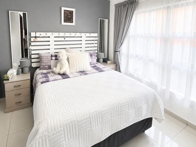 A well-maintained bedroom featuring neutral tiled flooring, decorative ceiling cornicing, and a large window allowing for ample natural light.