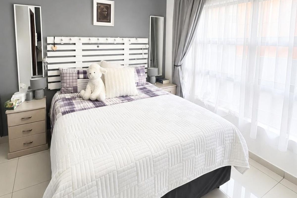 A well-maintained bedroom featuring neutral tiled flooring, decorative ceiling cornicing, and a large window allowing for ample natural light.