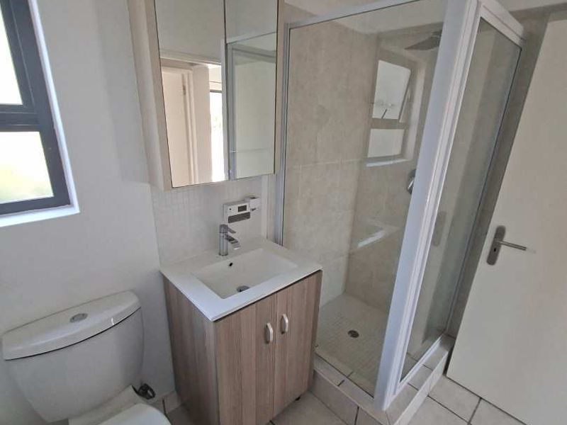 A clean and functional bathroom featuring a modern vanity, mirrored medicine cabinet, toilet, and a glass-enclosed shower with tiled flooring.