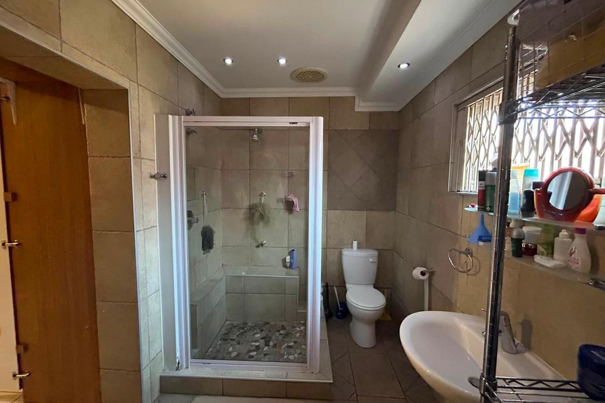 A functional bathroom featuring a glass-enclosed shower, pedestal basin, and toilet, finished with neutral wall and floor tiling and recessed ceiling lighting.