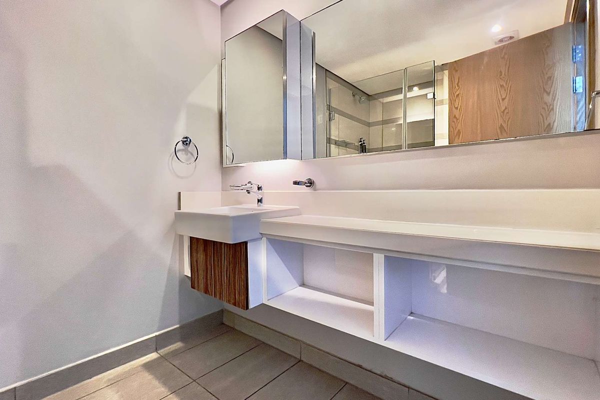 Modern bathroom vanity featuring a sleek countertop, integrated basin, and large wall-mounted mirror with built-in storage cabinetry.