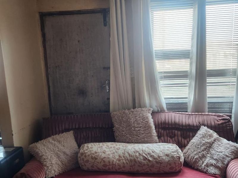 A living room area featuring a window with venetian blinds and a curtain rod, showing signs of wear on the door and wall surfaces.
