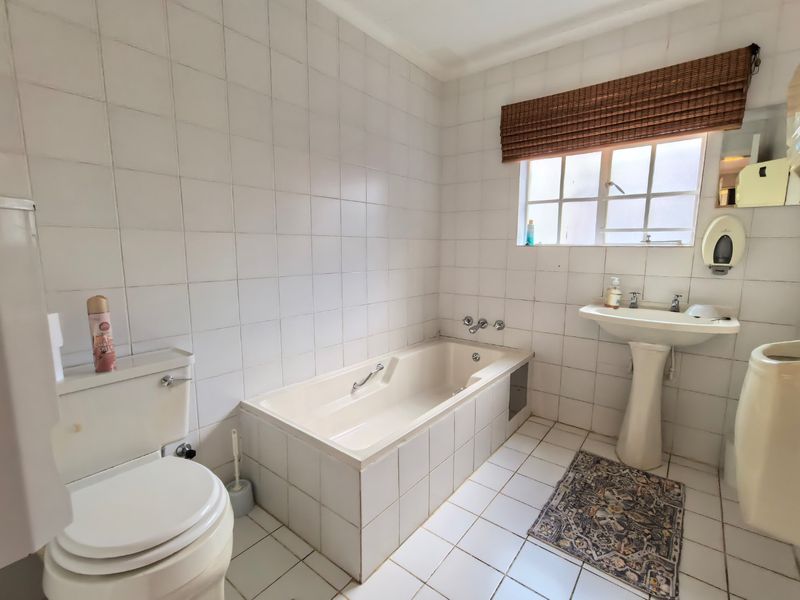 A dated bathroom featuring a built-in bathtub, pedestal basin, and toilet with white wall and floor tiling.