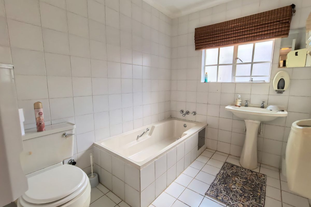 A dated bathroom featuring a built-in bathtub, pedestal basin, and toilet with white wall and floor tiling.