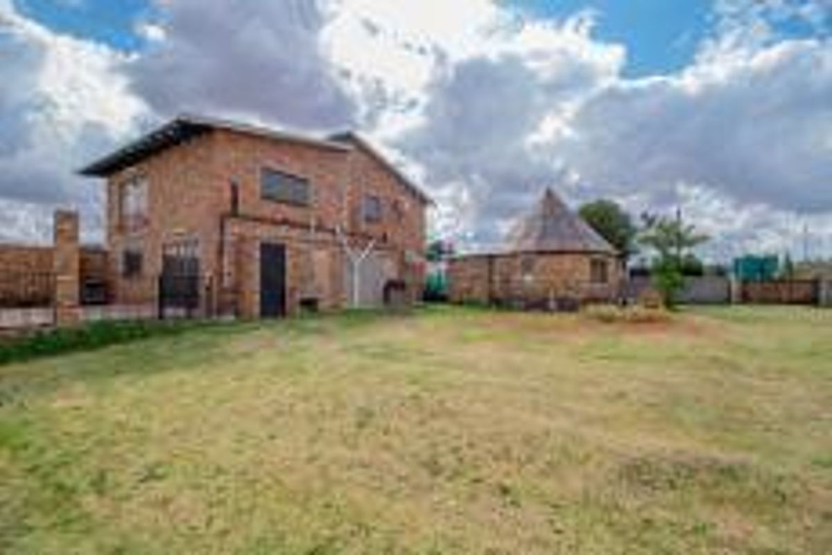 A view of the rear exterior of the farm property, featuring a two-story brick building and a separate circular structure set within a spacious yard.