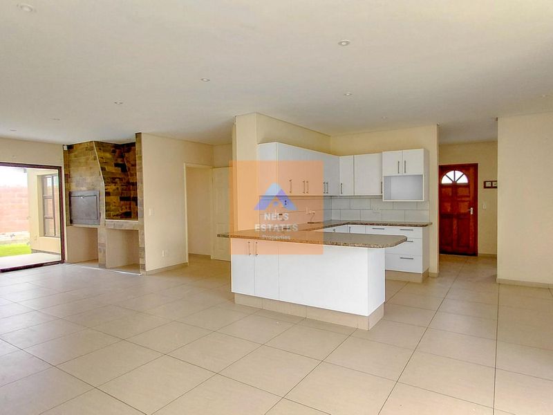 Spacious open-plan living area featuring a modern kitchen with stone countertops, built-in cabinetry, and an integrated indoor braai, leading to an outdoor patio.