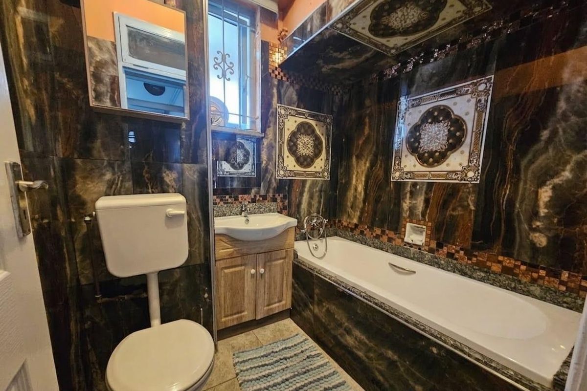 A compact bathroom featuring dark marble-effect wall tiling, a built-in vanity with a washbasin, a standard bathtub, and a toilet.