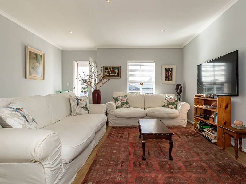A bright and comfortable living room featuring laminate flooring, recessed downlighting, and neutral wall finishes, providing a versatile space for relaxation.