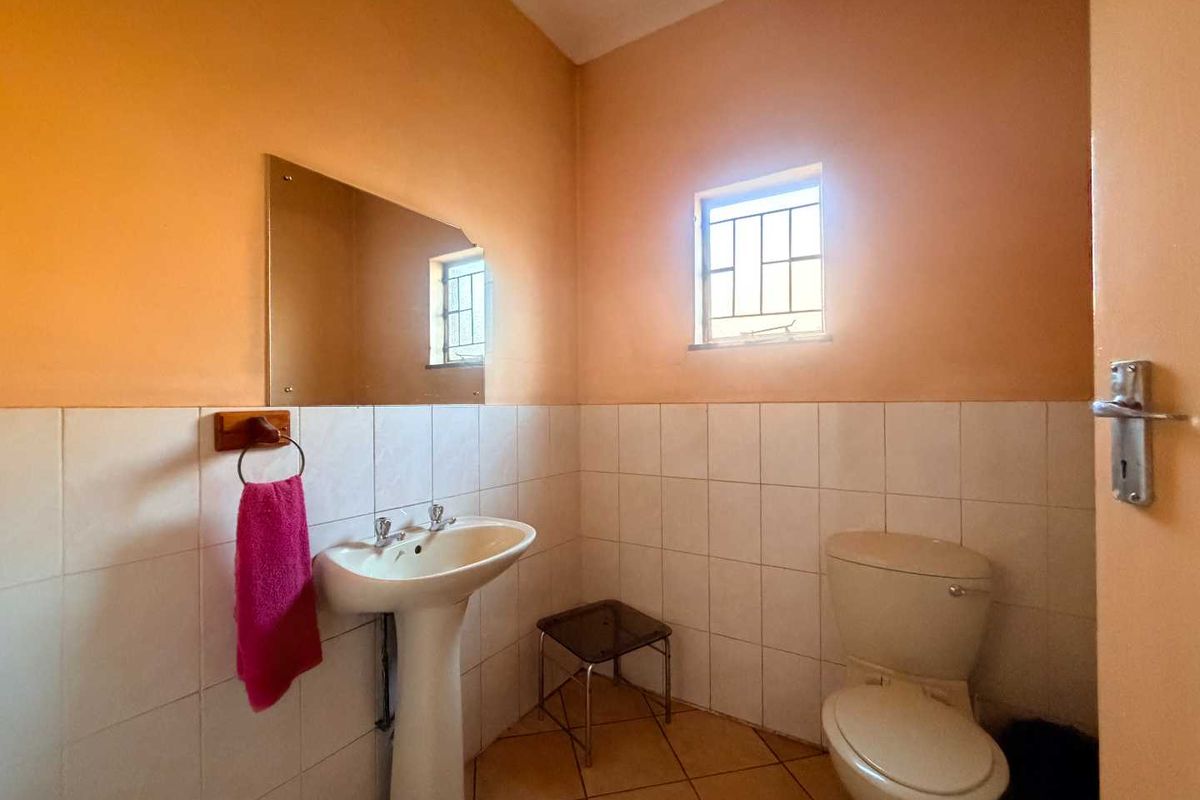 A functional bathroom featuring a pedestal sink, toilet, wall-mounted mirror, and tiled finishes, providing a clean and practical space.