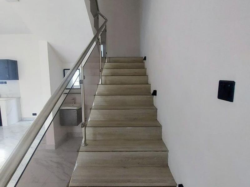 A modern staircase featuring wood-look treads, a sleek glass balustrade with stainless steel handrails, and integrated wall-mounted step lighting.