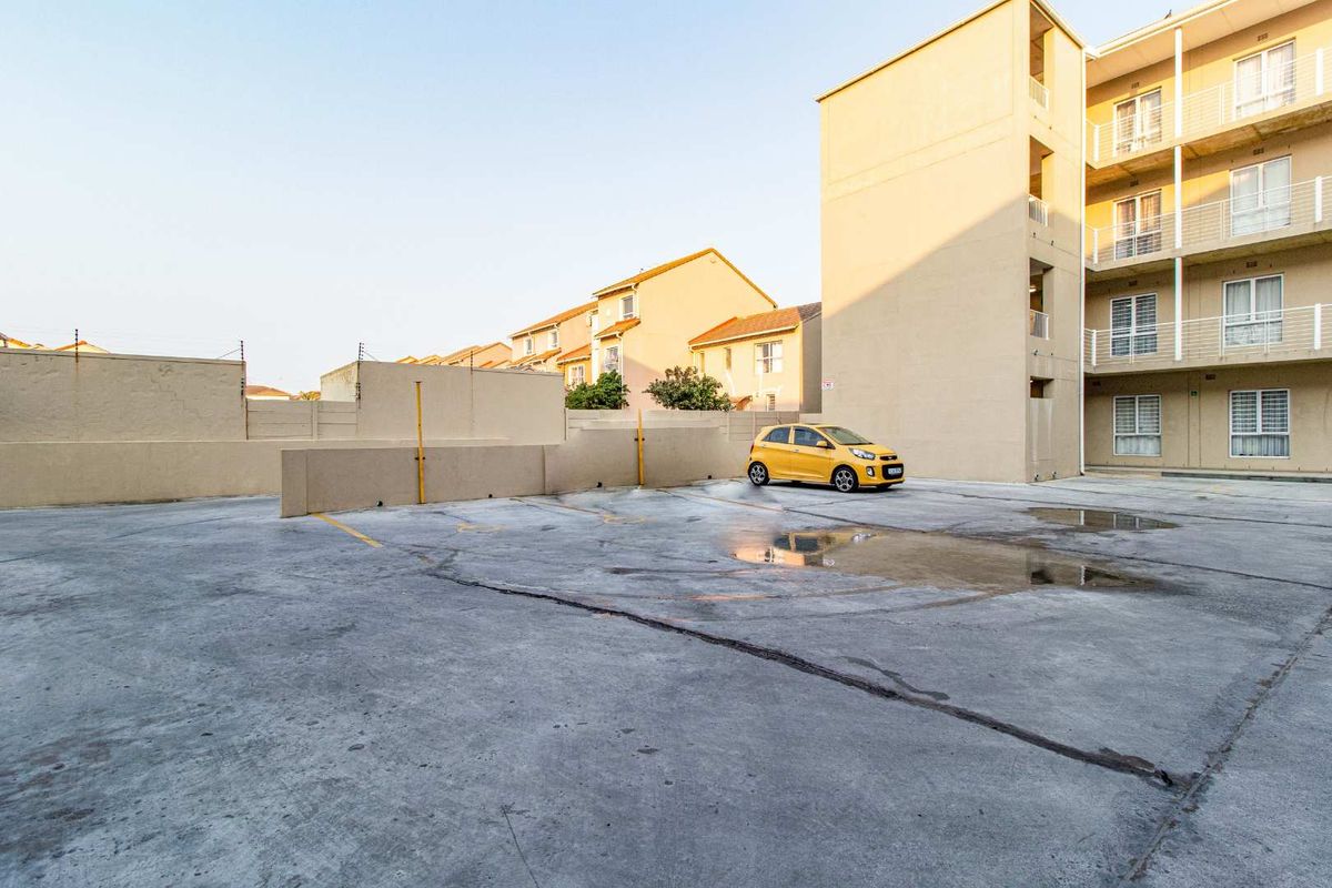 Exterior view of the apartment complex parking area featuring concrete paving and perimeter boundary walls.