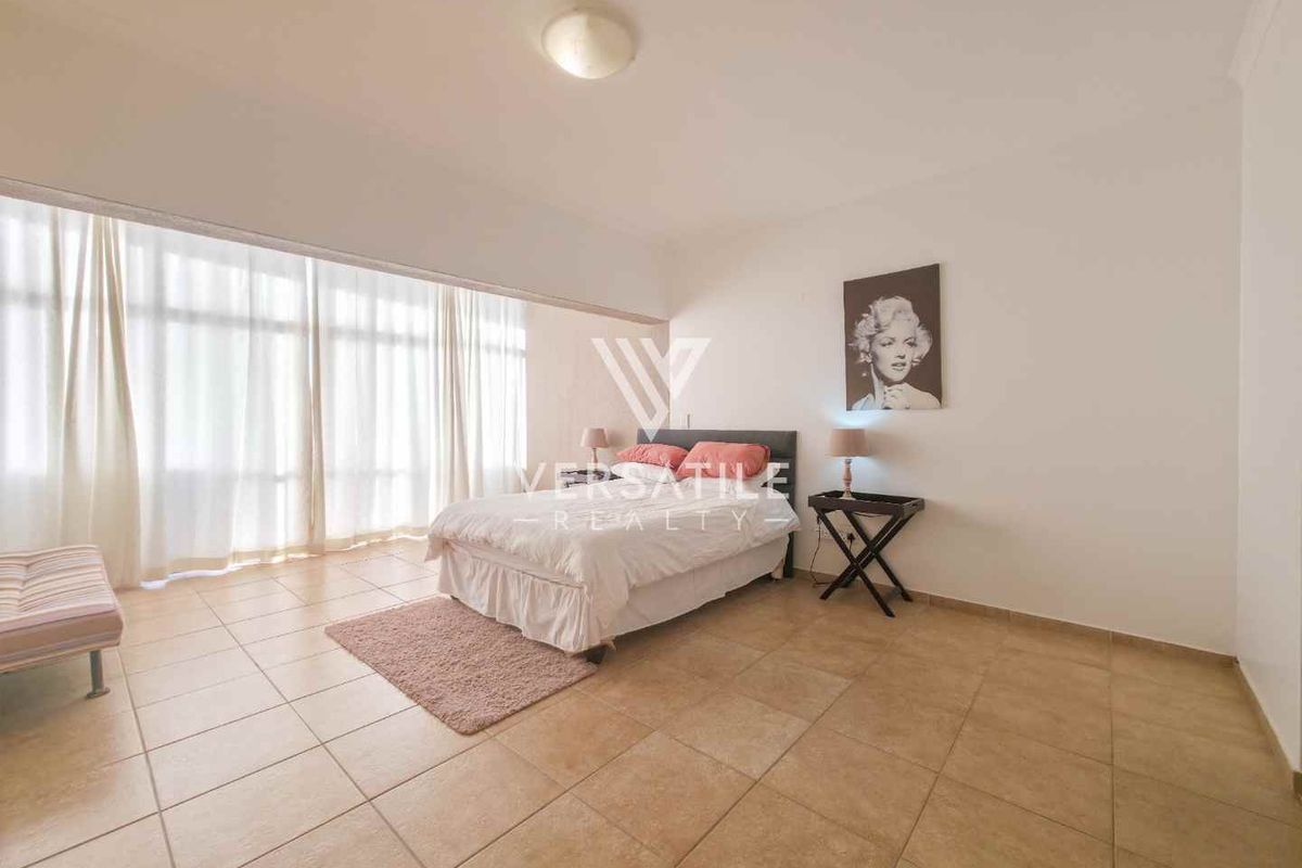 Spacious bedroom featuring large floor-to-ceiling windows with sheer curtains and neutral tiled flooring.