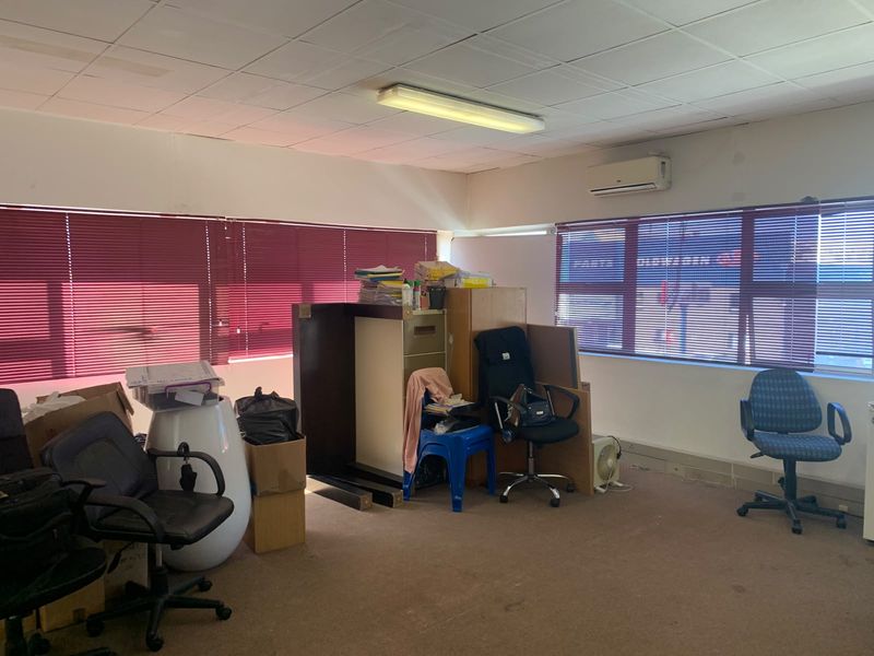 A functional office space featuring a suspended ceiling, split-system air conditioning, and large windows with venetian blinds, currently requiring cosmetic updates.