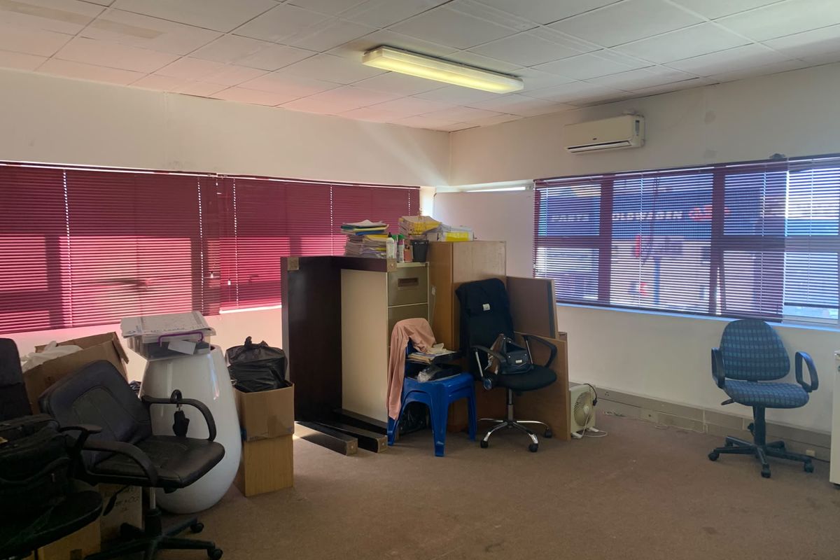 A functional office space featuring a suspended ceiling, split-system air conditioning, and large windows with venetian blinds, currently requiring cosmetic updates.
