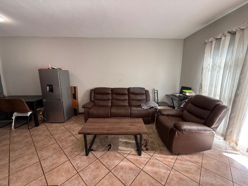 A spacious living area featuring neutral wall finishes, tiled flooring, and a sliding glass door providing natural light.
