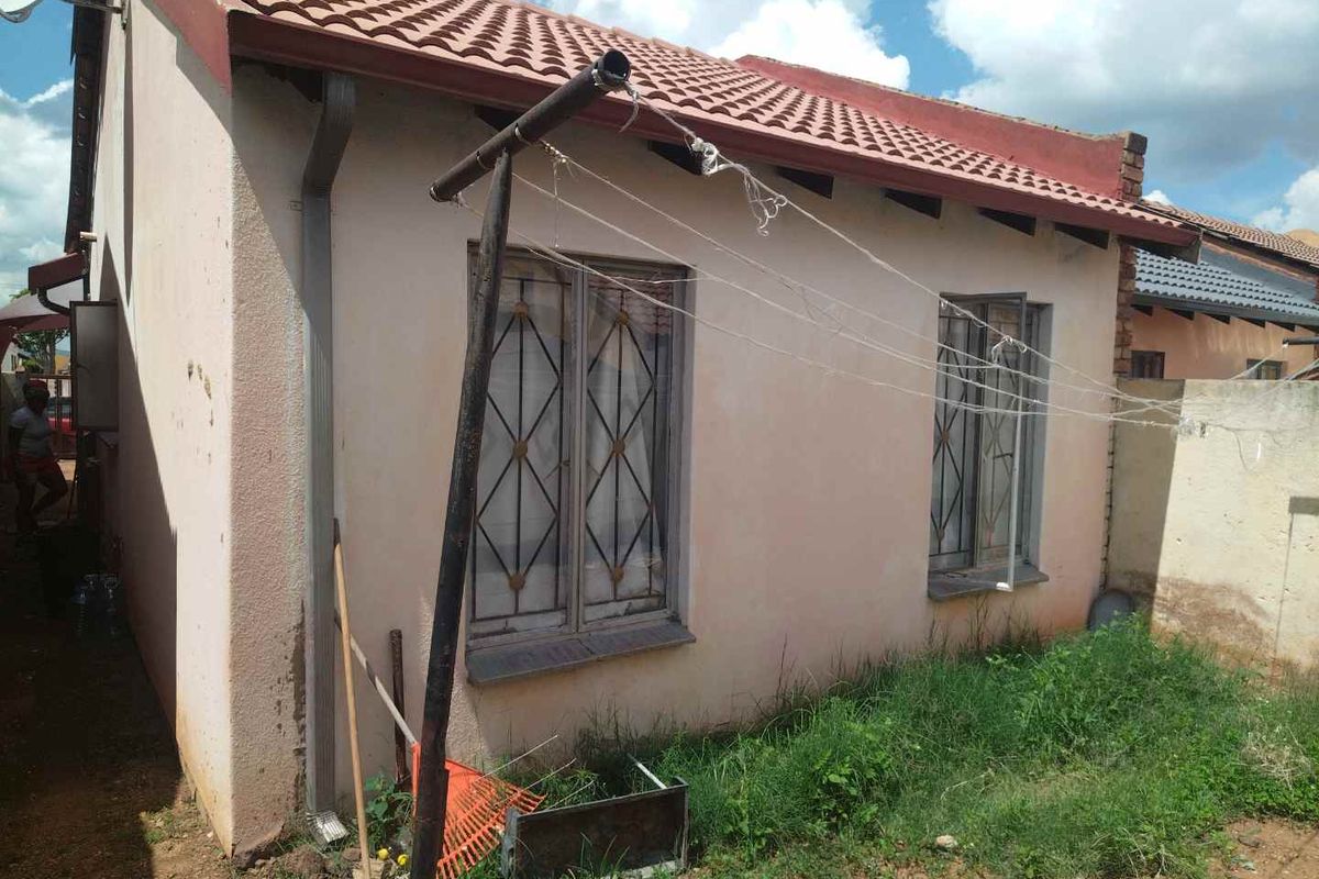 Rear exterior view of the house featuring a tiled roof, metal security window bars, and a basic drainage system.