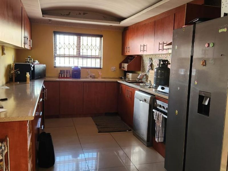 A functional kitchen featuring wood-tone cabinetry, tiled flooring, and a window with security bars, offering a practical layout for daily meal preparation.