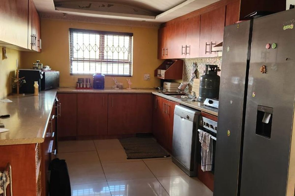 A functional kitchen featuring wood-tone cabinetry, tiled flooring, and a window with security bars, offering a practical layout for daily meal preparation.
