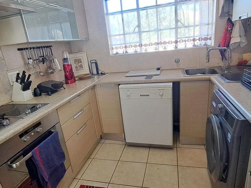 A functional kitchen featuring light wood-finish cabinetry, a gas hob with extractor, built-in oven, and tiled finishes throughout.