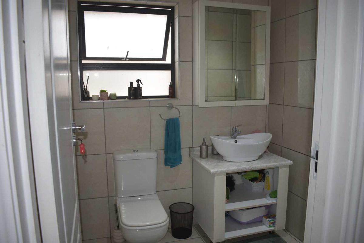 A compact bathroom featuring a modern vessel sink vanity, a wall-mounted medicine cabinet, a toilet, and neutral wall tiling.