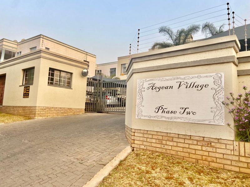 Entrance view of Aegean Village Phase Two, featuring a secure gated access point with electric fencing and paved driveway.