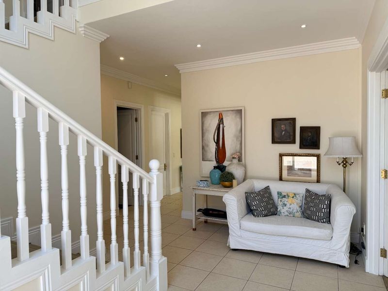 A bright and welcoming entrance hall featuring tiled flooring, a classic white staircase with balustrade, and recessed ceiling lighting.